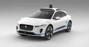 Vozidlo s logom spoločnosti Waymo, elektrické auto na autonómne riadenie, biele s modrými akcentmi, na neutrálnej šedej pozadí, technológia autonómneho jazdenia, moderný dizajn, bezpečnostné prvky.